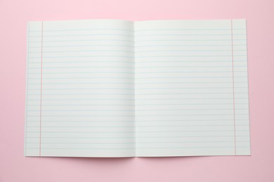 Photo of Open copybook on pink background, top view. School stationery