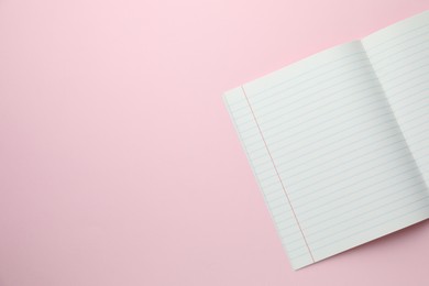 Photo of Open copybook on pink background, top view. School stationery