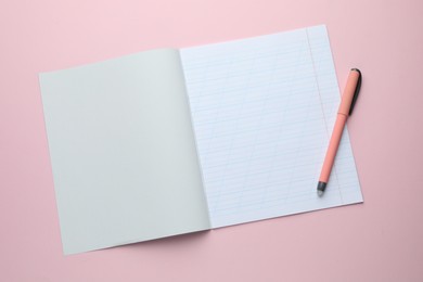 Photo of Open copybook and pen on pink background, top view. School stationery