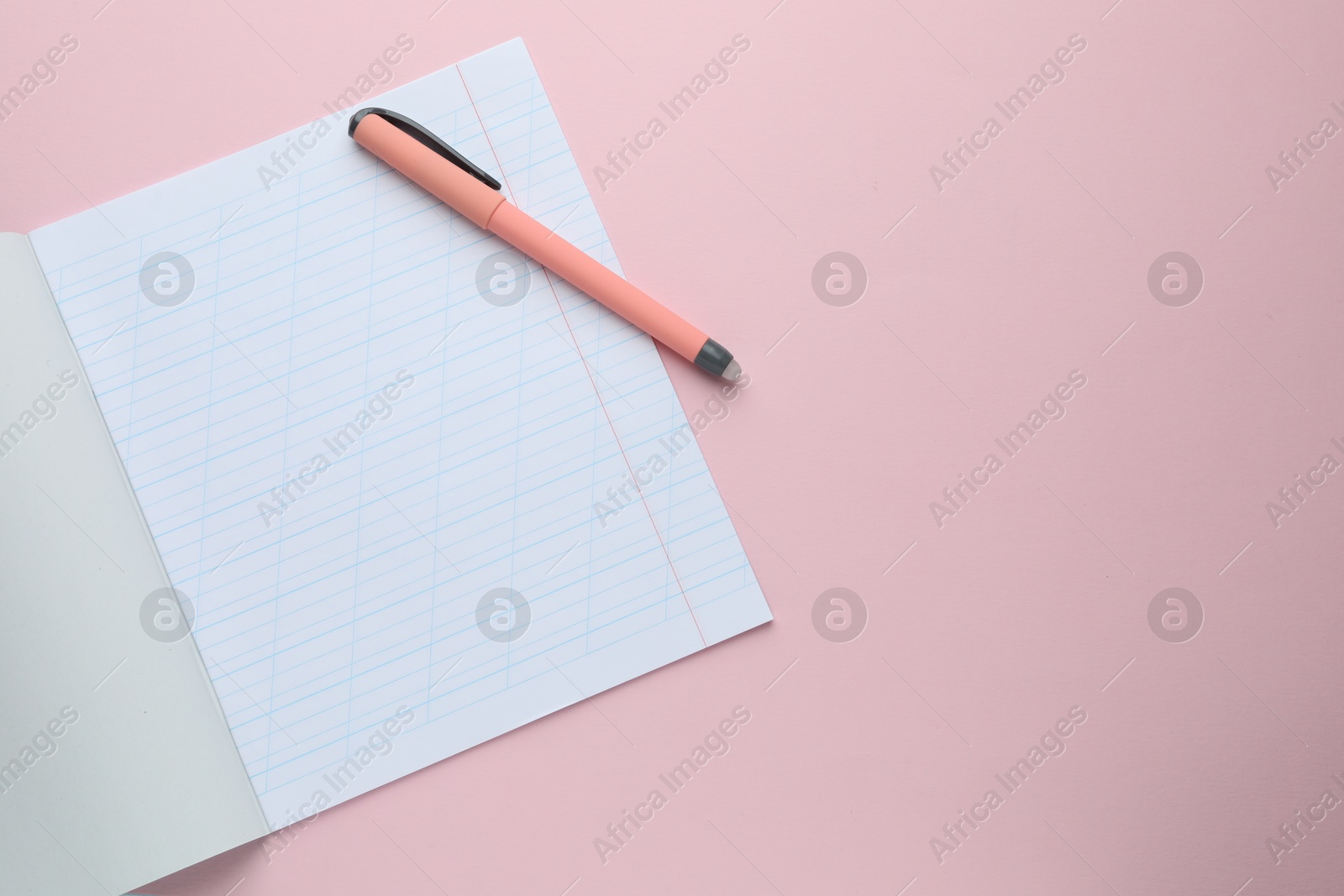 Photo of Open copybook and pen on pink background, top view. School stationery