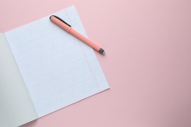 Photo of Open copybook and pen on pink background, top view. School stationery