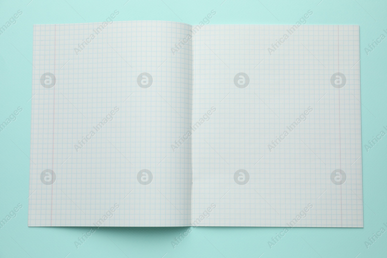 Photo of Open copybook with checkered sheets of paper on light blue background, top view. School stationery