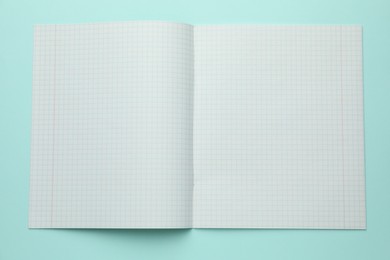 Photo of Open copybook with checkered sheets of paper on light blue background, top view. School stationery