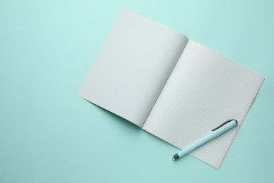 Photo of Open copybook with checkered sheets of paper and pen on light blue background, top view. School stationery