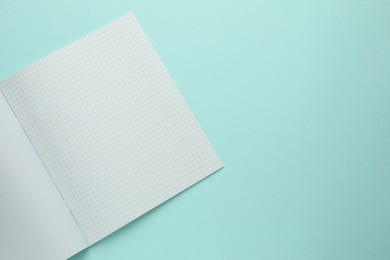 Photo of Open copybook with checkered sheets of paper on light blue background, top view. School stationery