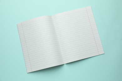 Photo of Open copybook on light blue background, top view. School stationery