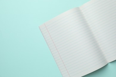 Photo of Open copybook on light blue background, top view. School stationery. Space for text