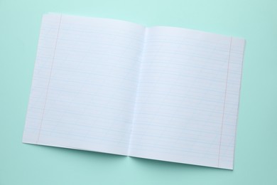 Photo of Open copybook on light blue background, top view. School stationery