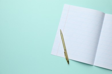 Photo of Open copybook and pen on light blue background, top view. School stationery