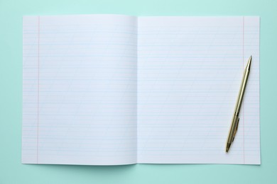 Photo of Open copybook and pen on light blue background, top view. School stationery