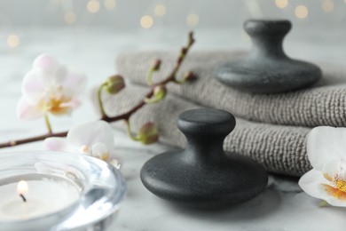 Spa stones, orchid flowers, towels and burning candle on white marble table, closeup