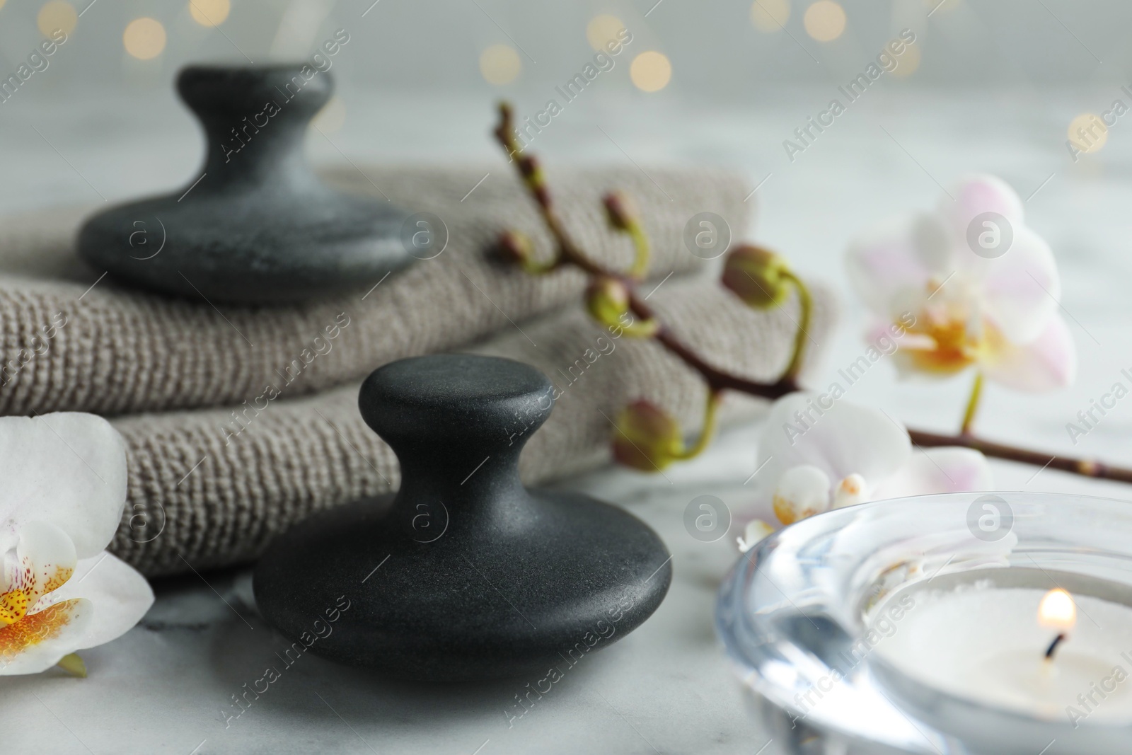 Photo of Spa stones, orchid flowers, towels and burning candle on white marble table, closeup