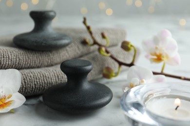 Photo of Spa stones, orchid flowers, towels and burning candle on white marble table, closeup