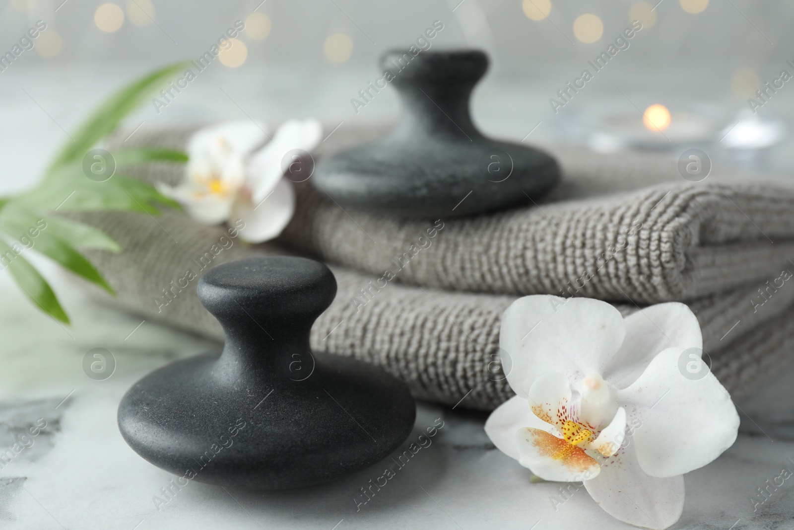 Photo of Spa stones, orchid flowers, palm leaf and towels on white marble table, closeup