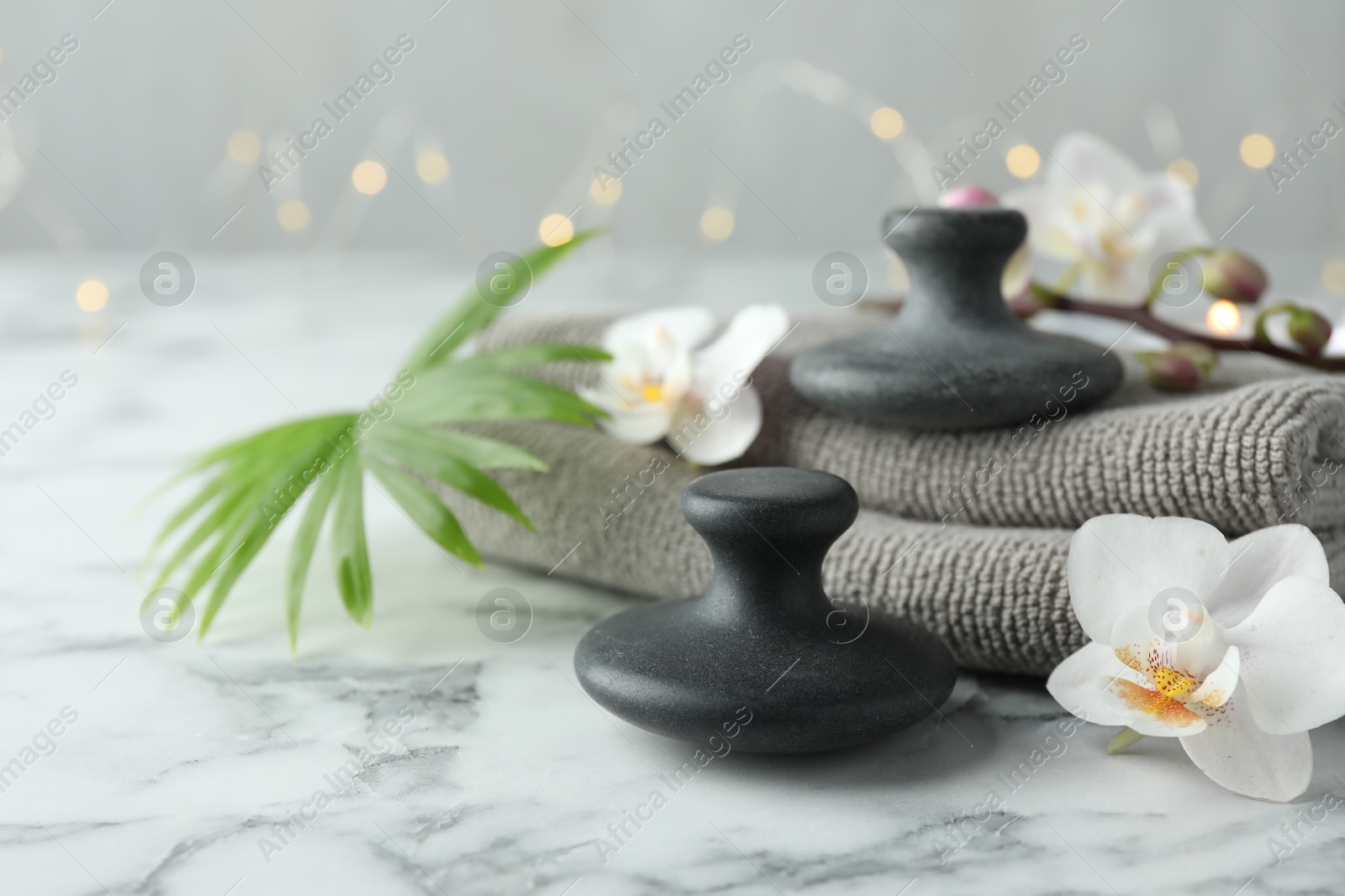 Photo of Spa stones, orchid flowers, towels and palm leaf on white marble table, closeup