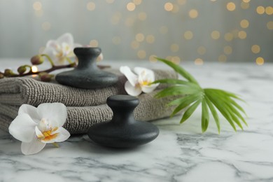 Spa stones, orchid flowers, towels and palm leaf on white marble table, closeup