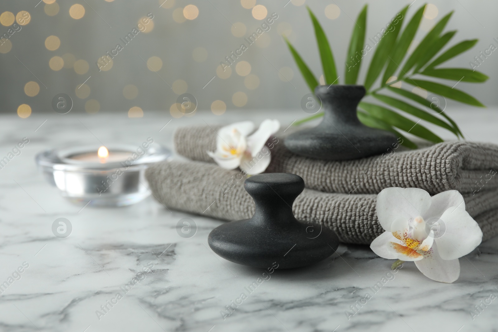 Photo of Spa stones, orchid flowers, towels, burning candle and leaf on white marble table, closeup