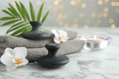 Photo of Spa stones, orchid flowers, towels, burning candle and leaf on white marble table, closeup