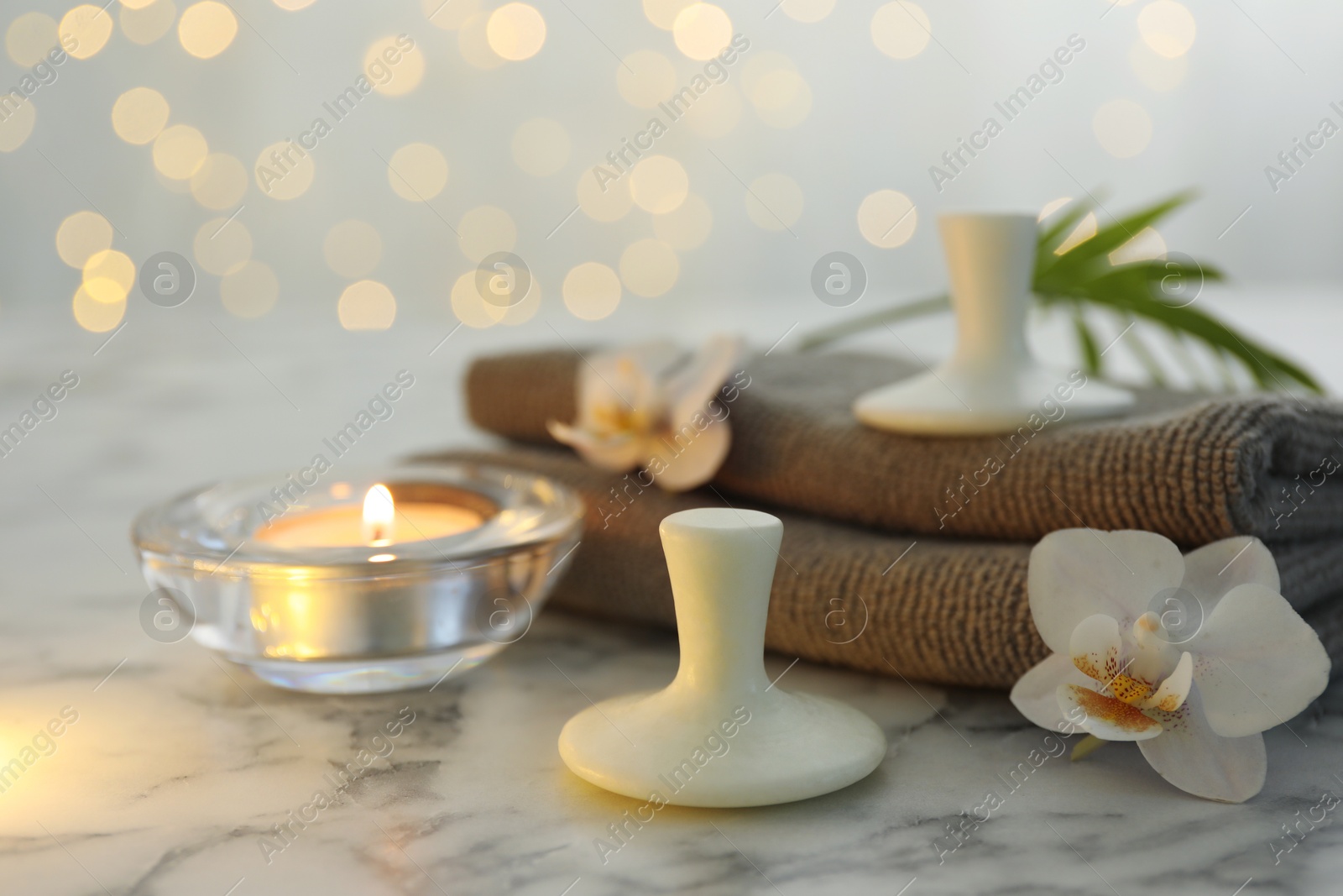 Photo of Spa stones, orchid flowers, towels and burning candle on white marble table, closeup