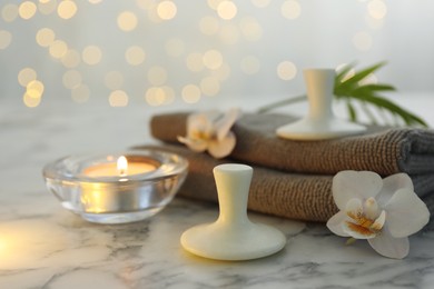 Photo of Spa stones, orchid flowers, towels and burning candle on white marble table, closeup