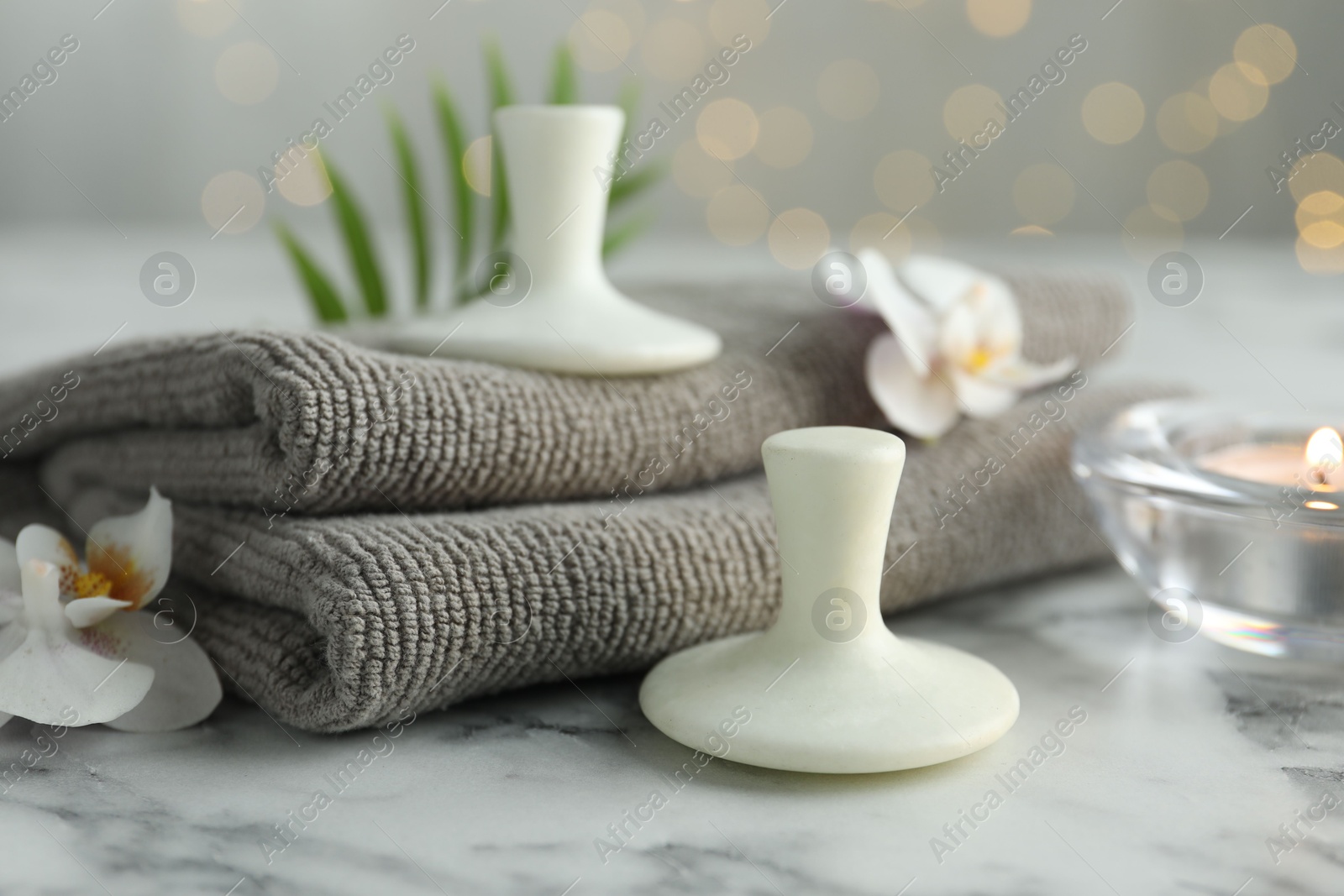 Photo of Spa stones, orchid flowers, towels and burning candle on white marble table, closeup