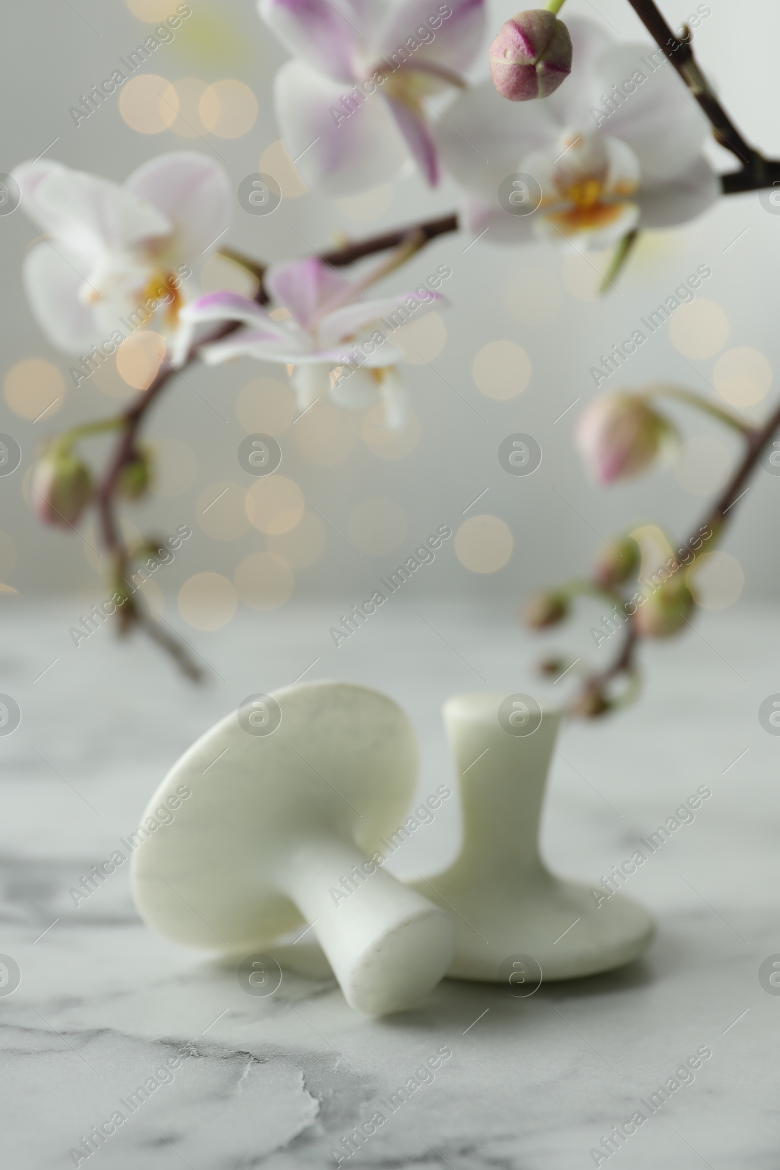 Photo of Spa stones on white marble table and orchid branch against blurred lights, closeup