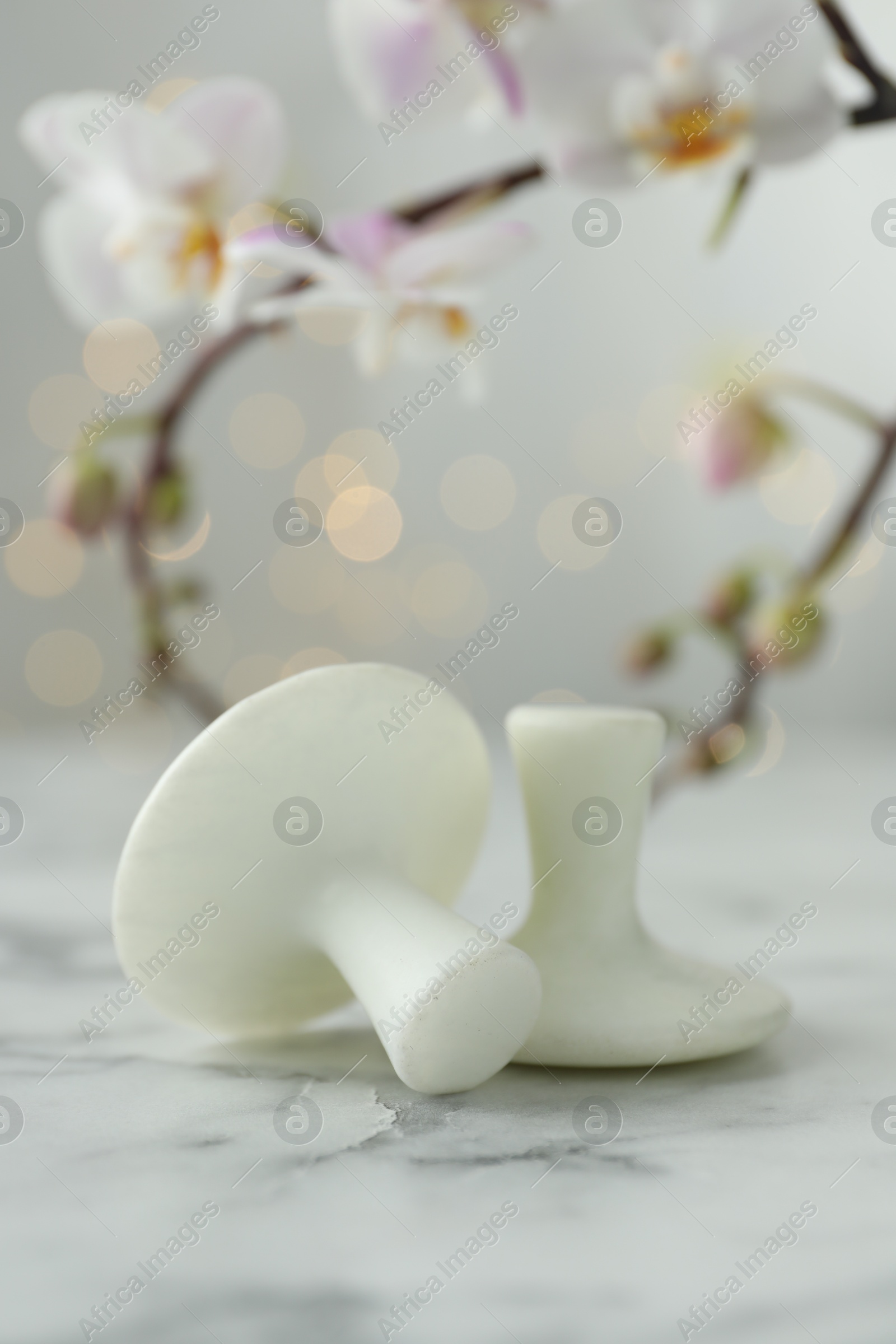 Photo of Spa stones on white marble table and orchid branch against blurred lights, closeup