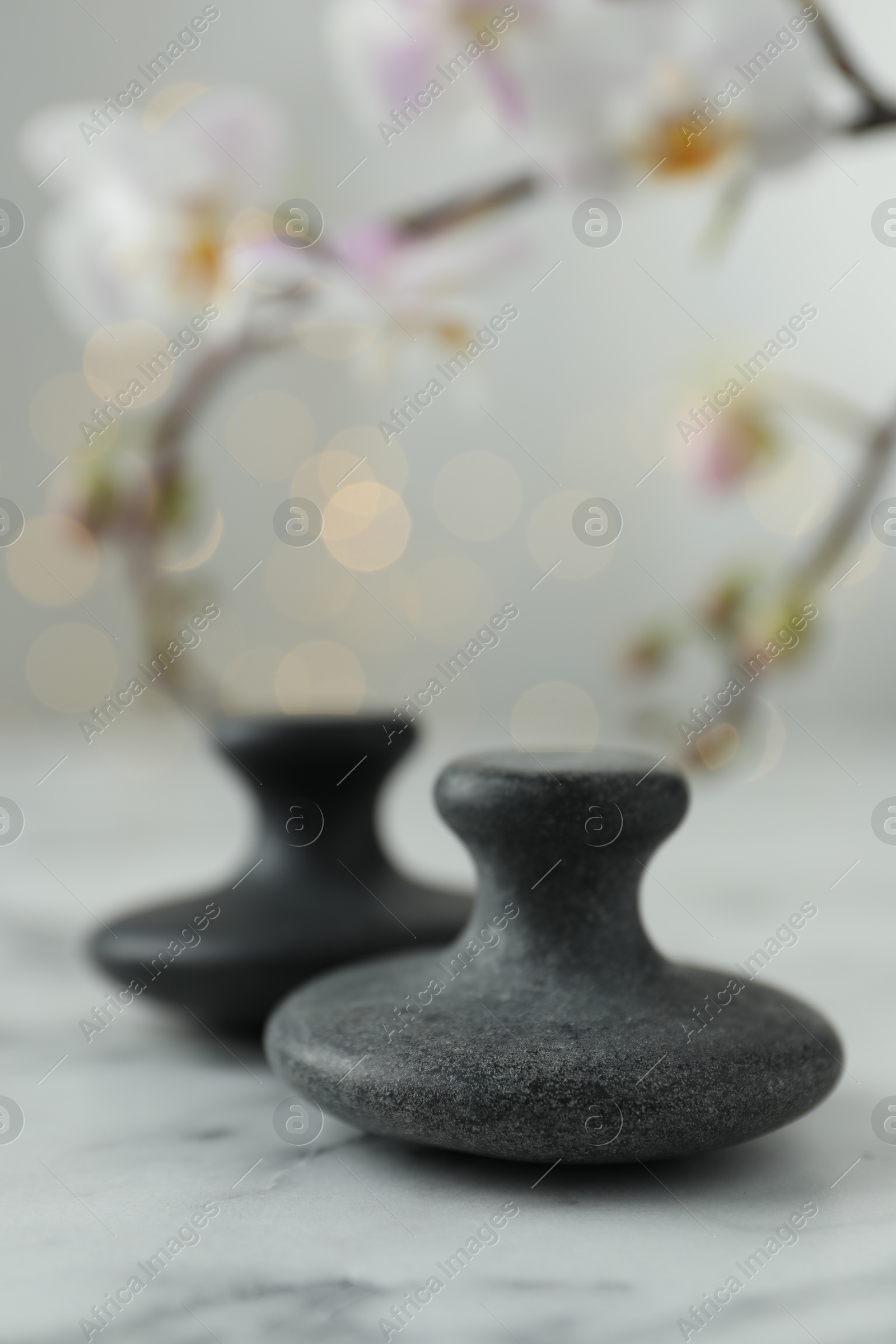 Photo of Spa stones on white marble table and orchid branch against blurred lights, closeup