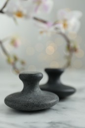 Spa stones on white marble table and orchid branch against blurred lights, closeup