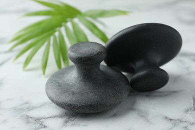 Photo of Spa stones and green palm leaf on white marble table, closeup