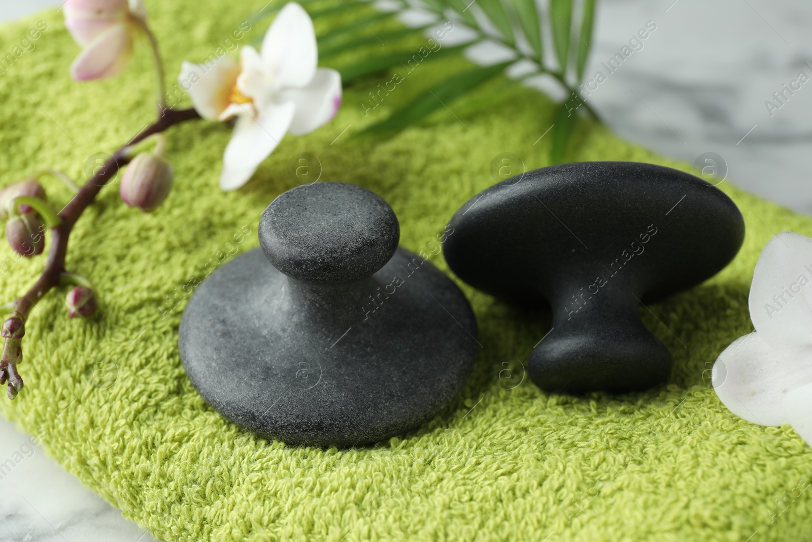 Photo of Spa stones, orchid branch, palm leaf and towel on table, closeup