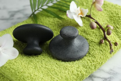 Photo of Spa stones, orchid branch, palm leaf and towel on white marble table, closeup