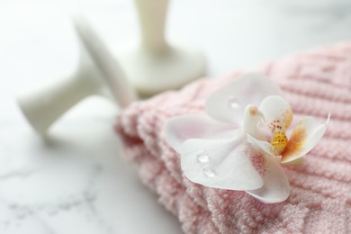 Photo of Orchid flower, spa stones and towel on white marble table, closeup