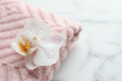 Photo of Orchid flower and towel on white marble table, closeup. Space for text