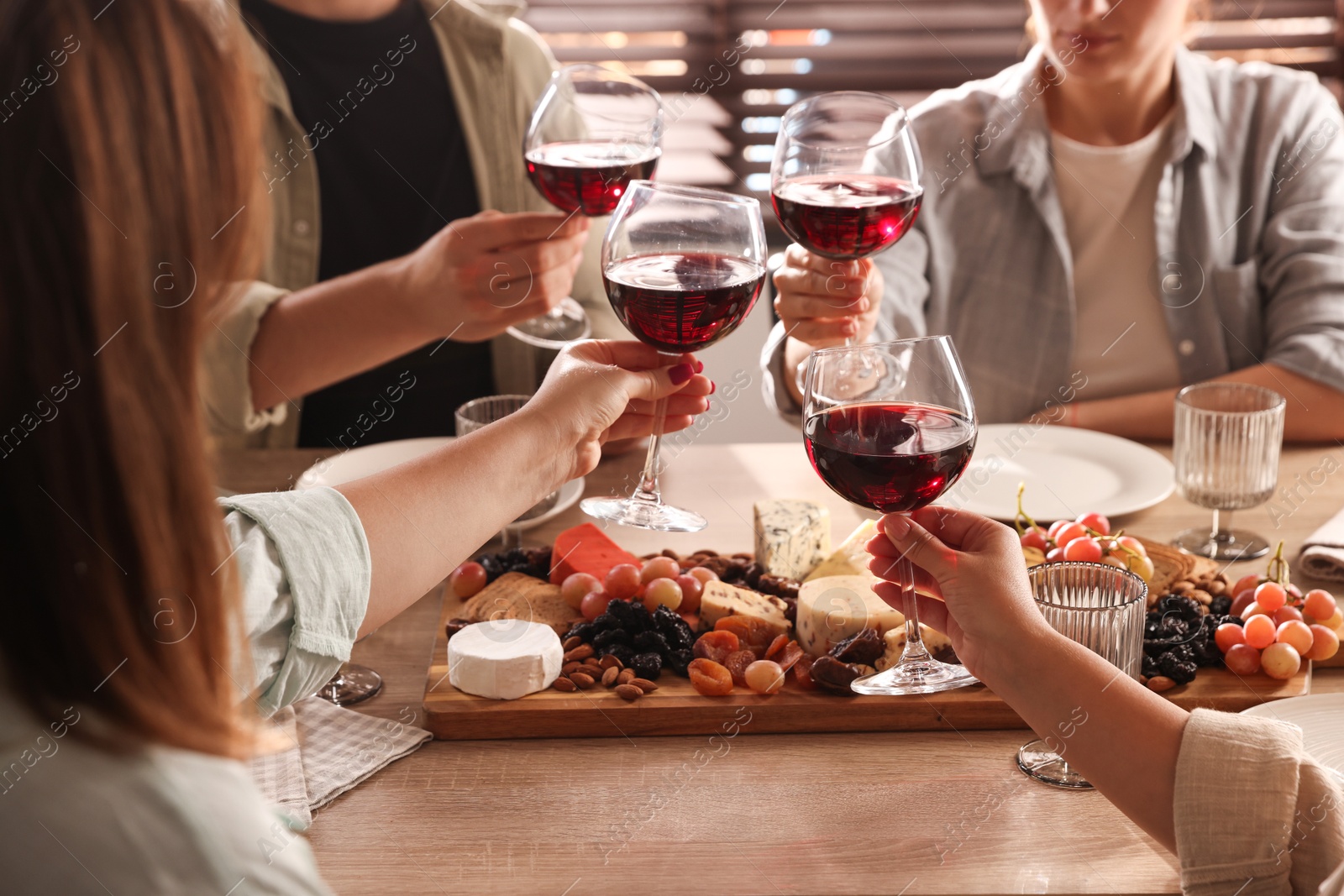 Photo of People clinking glasses of red wine at served table, closeup