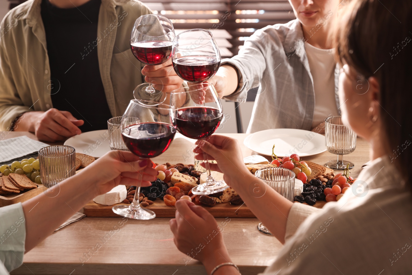 Photo of People clinking glasses of red wine at served table, closeup