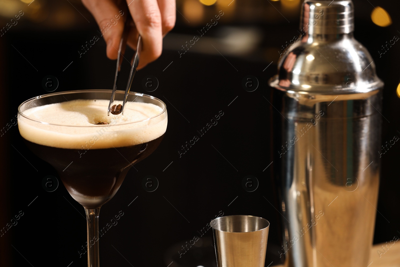 Photo of Bartender putting coffee bean into glass with delicious espresso martini on black background, closeup