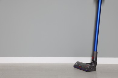 Photo of One cordless vacuum cleaner near grey wall indoors. Space for text