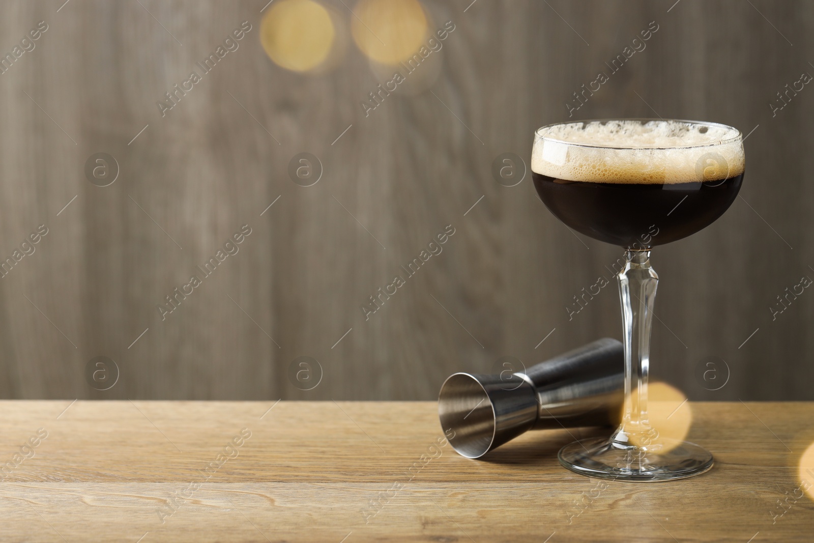 Photo of Delicious espresso martini with coffee beans in glass and jigger on wooden table. Space for text