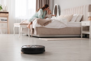 Photo of Mother spending time with her daughter in bedroom, focus on robotic vacuum cleaner