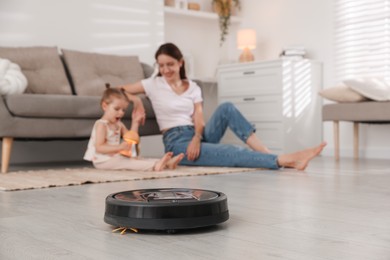 Photo of Mother spending time with her daughter in room, focus on robotic vacuum cleaner