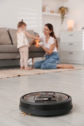 Photo of Mother spending time with her daughter in room, focus on robotic vacuum cleaner