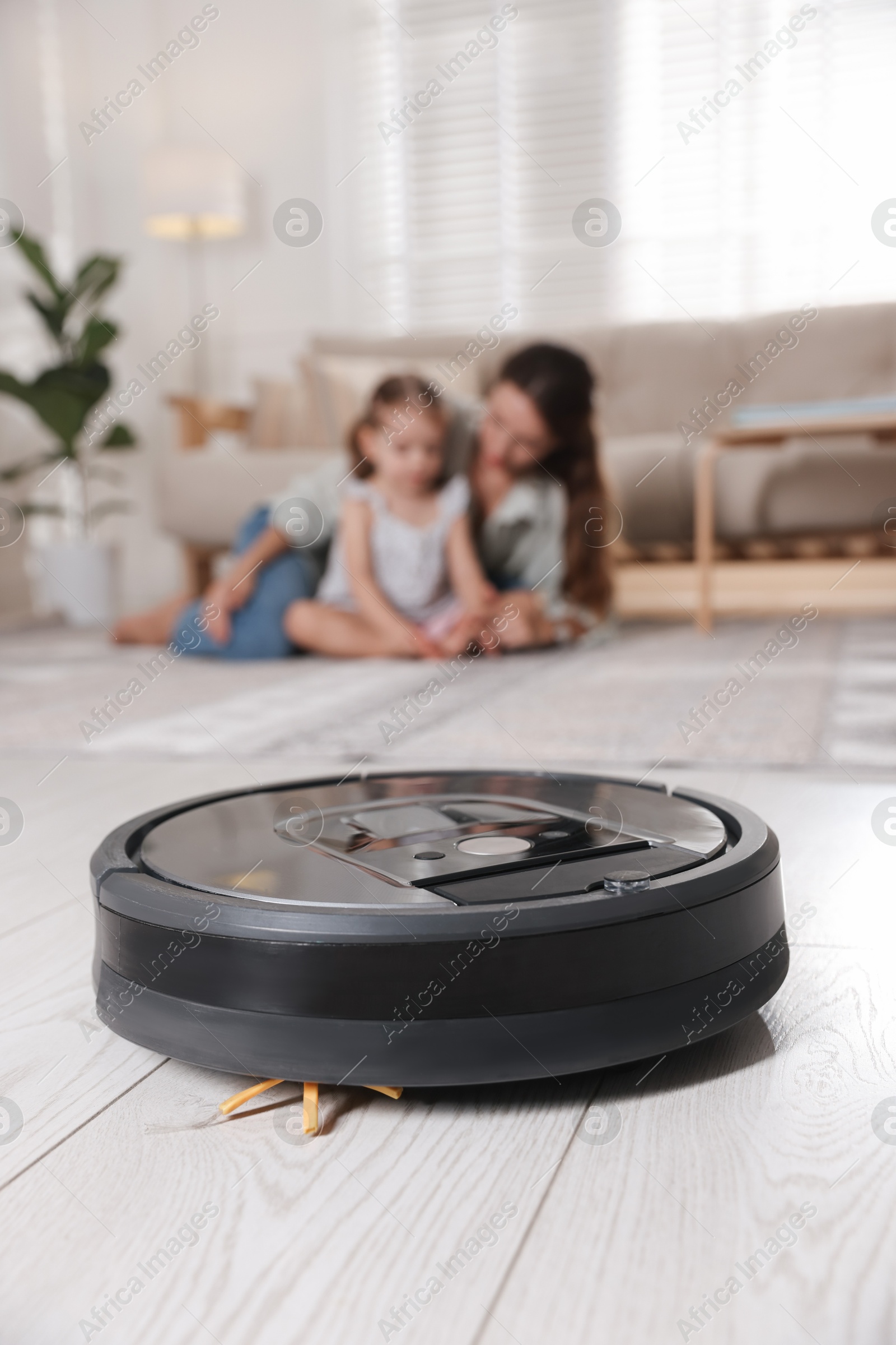 Photo of Mother spending time with her daughter in room, focus on robotic vacuum cleaner