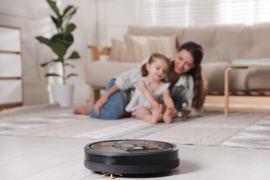 Photo of Mother spending time with her daughter in room, focus on robotic vacuum cleaner