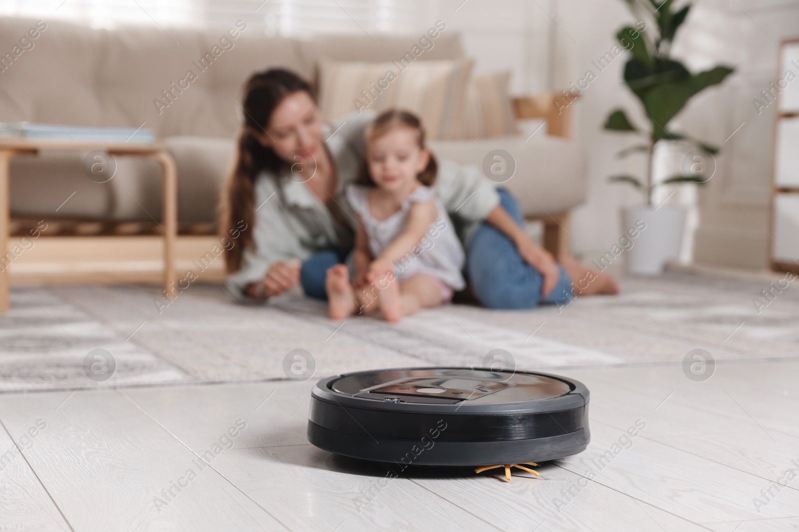 Photo of Mother spending time with her daughter in room, focus on robotic vacuum cleaner