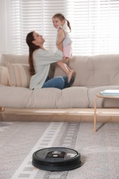 Photo of Mother spending time with her daughter in room, focus on robotic vacuum cleaner