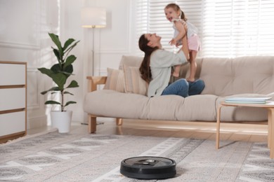 Photo of Mother spending time with her daughter in room, focus on robotic vacuum cleaner