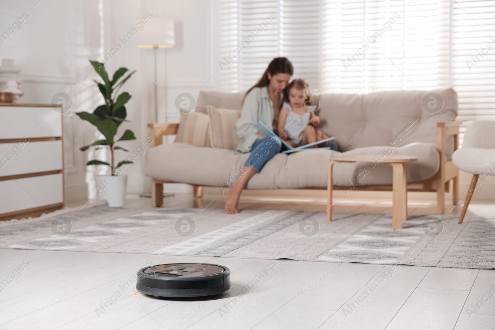 Photo of Mother spending time with her daughter in room, focus on robotic vacuum cleaner