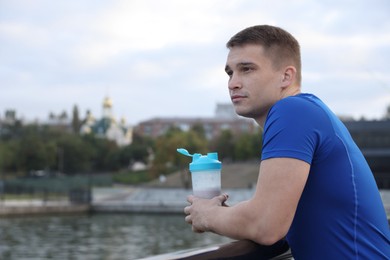 Photo of Athletic man with shaker of protein drink outdoors. Space for text