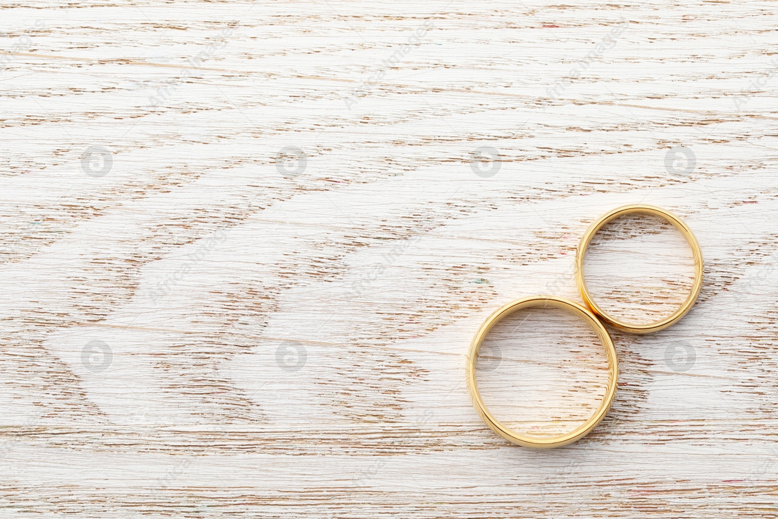 Photo of Beautiful golden wedding rings on wooden table, top view. Space for text